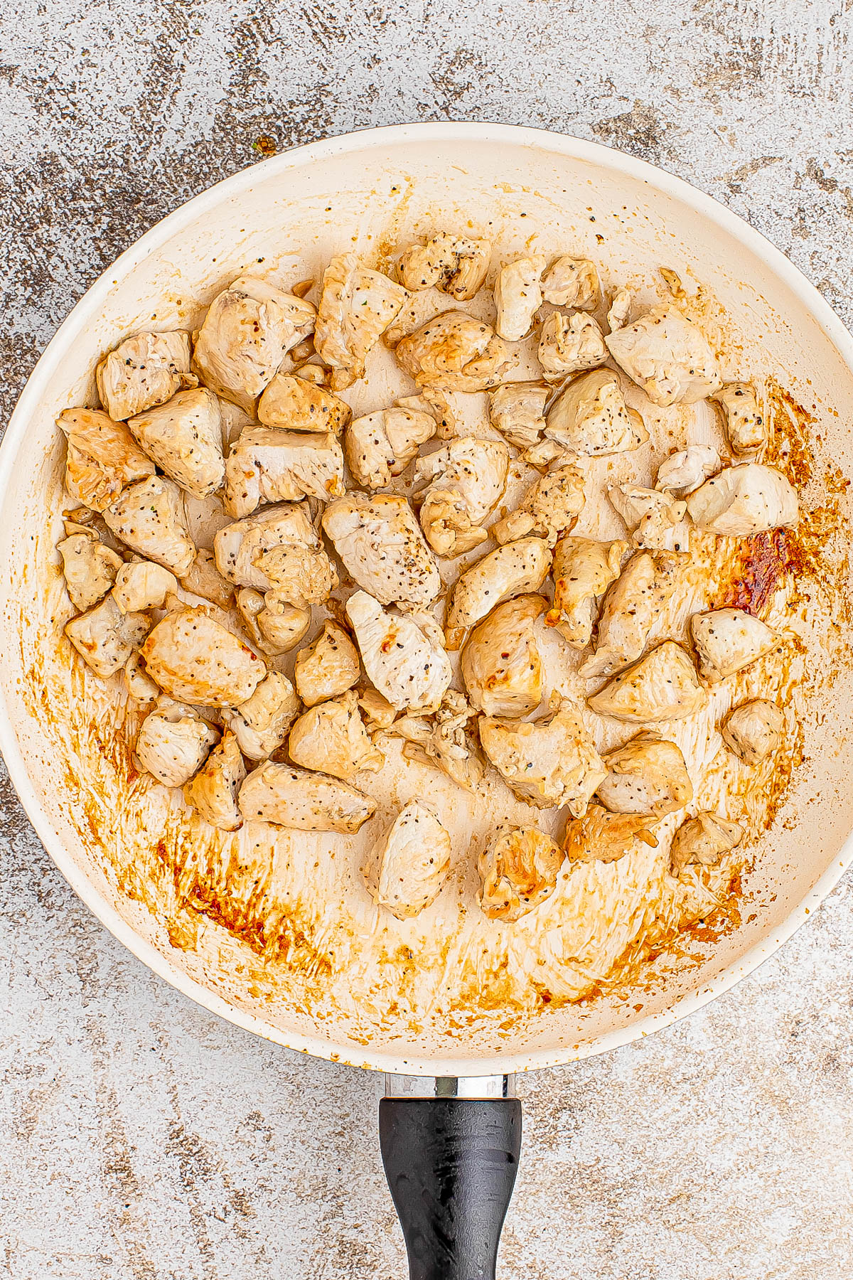 Cooked chicken pieces in a frying pan, seasoned with pepper and a light brown crust on some pieces.