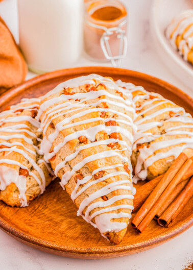 A wooden plate with glazed scones topped with icing and accompanied by cinnamon sticks.