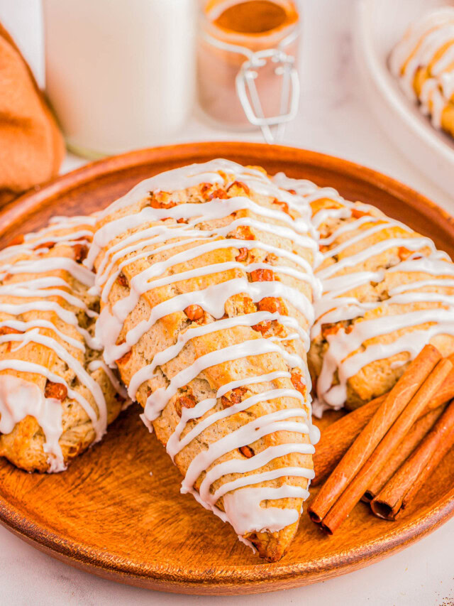 A wooden plate with glazed scones topped with icing and accompanied by cinnamon sticks.