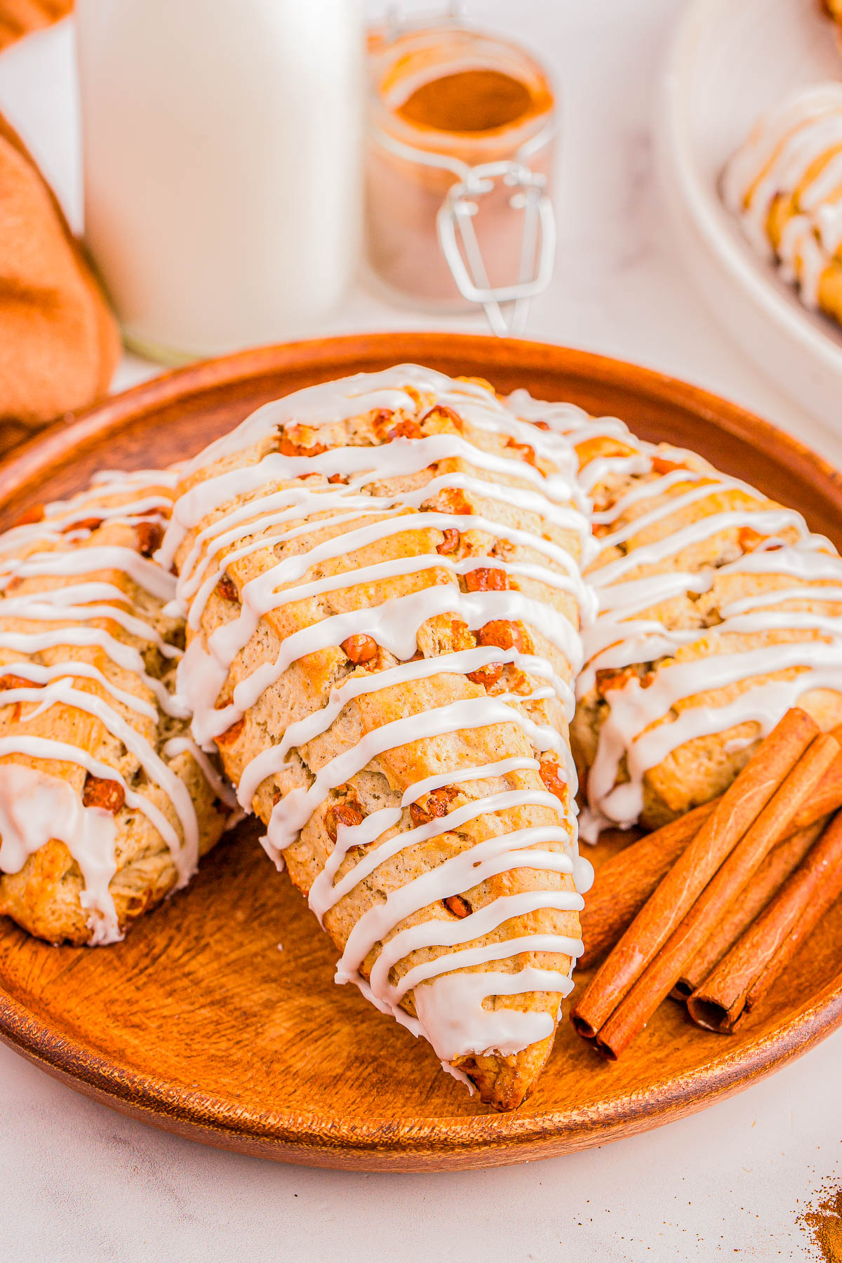 A wooden plate with glazed scones topped with icing and accompanied by cinnamon sticks.