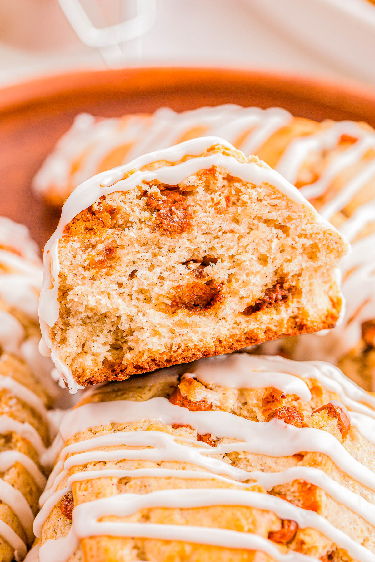 Close-up of cinnamon scones with white icing drizzled on top, one positioned upright showing a textured inside.