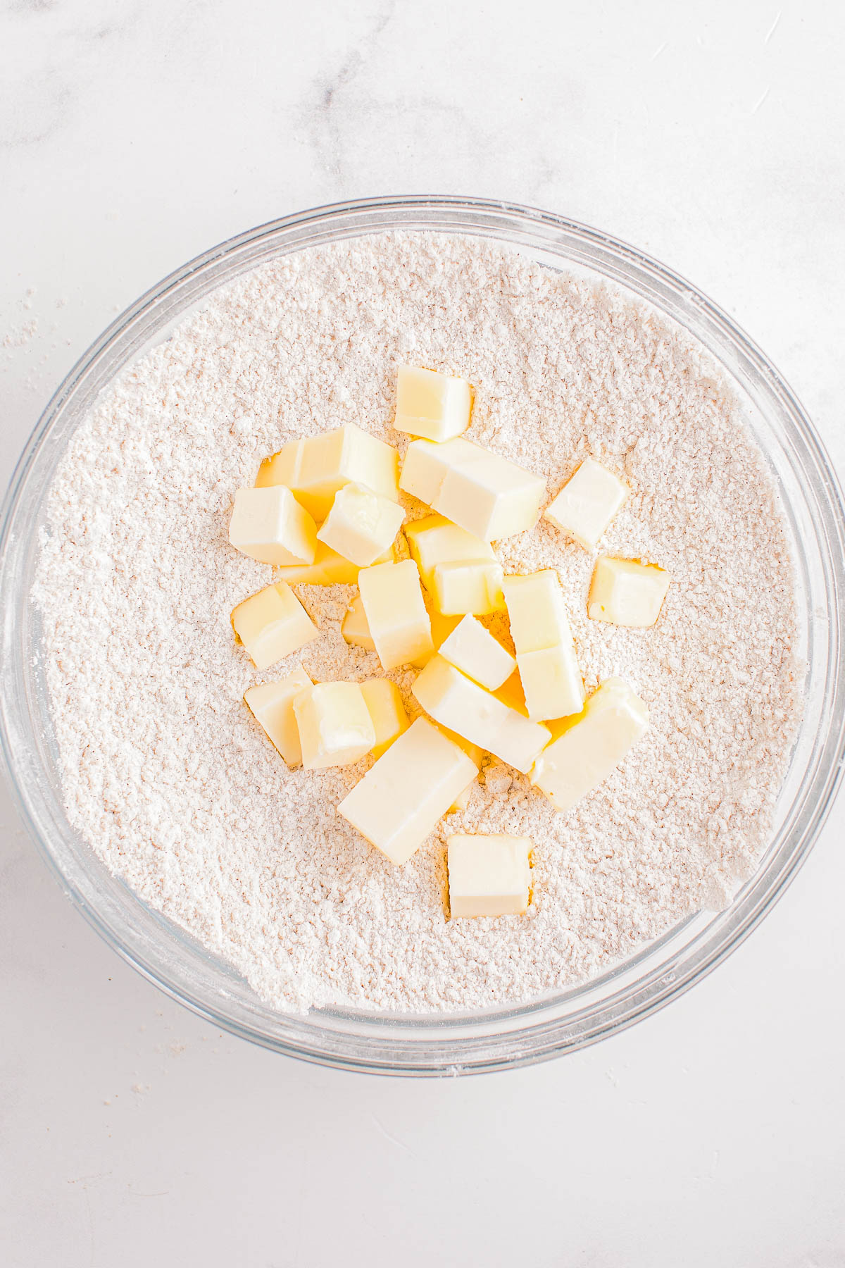 A glass bowl contains flour with cubes of butter on top.