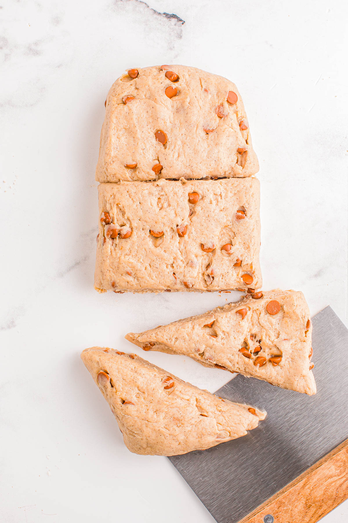 Sliced dough with chocolate chips on a marble surface, accompanied by a metal dough cutter.