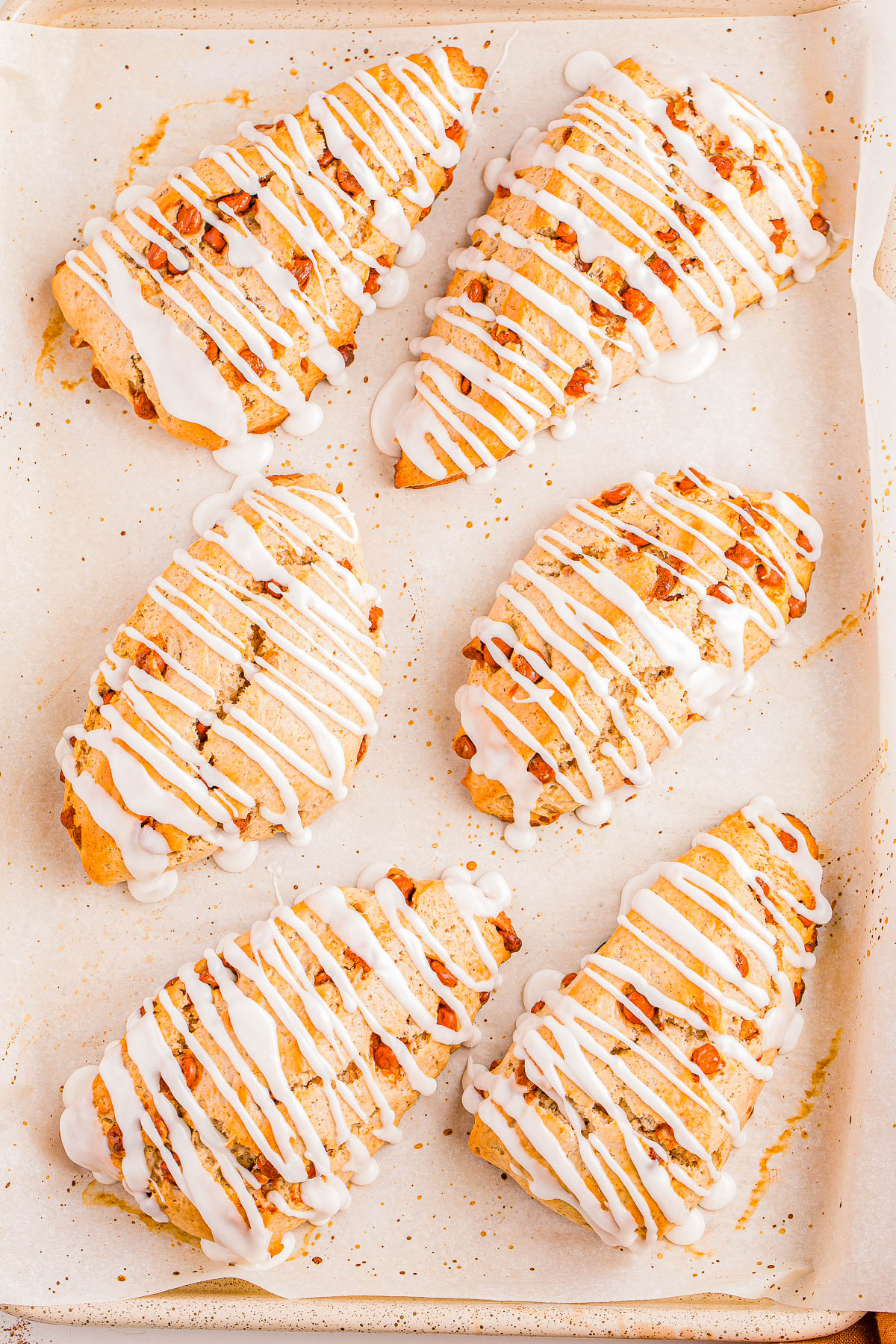 Six iced scones with nuts on a parchment-lined baking sheet.