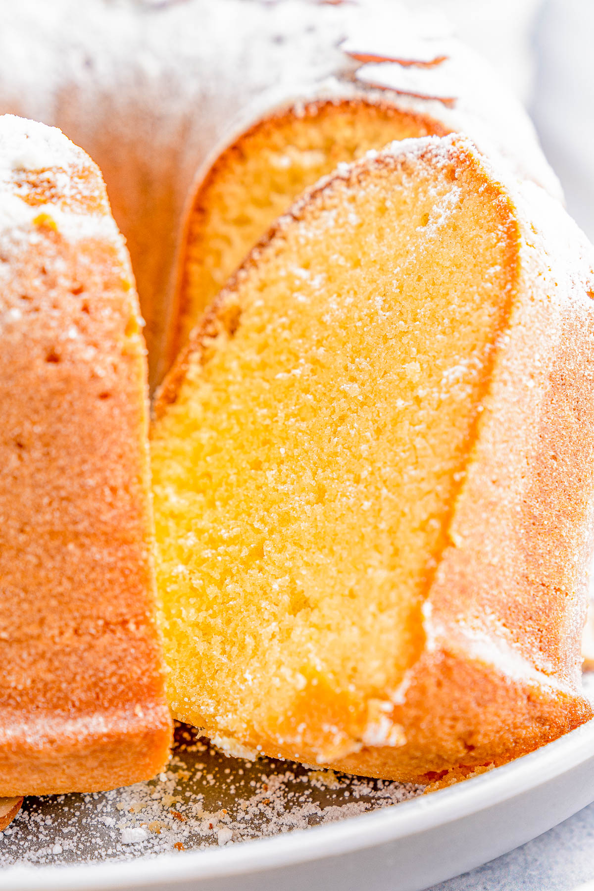 A close-up of a sliced bundt cake dusted with powdered sugar on a white plate.