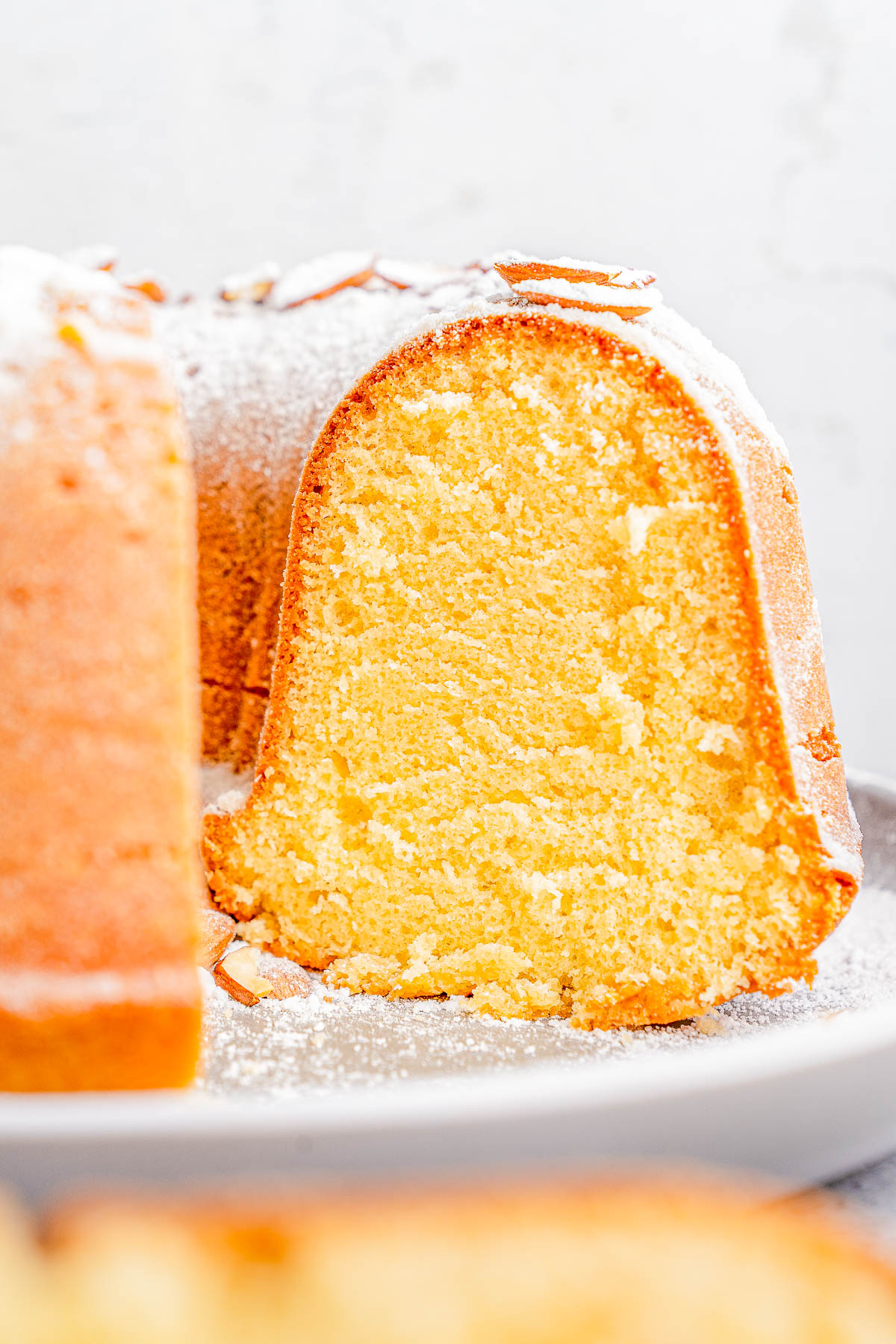 A close-up of a sliced Bundt cake dusted with powdered sugar on a plate.