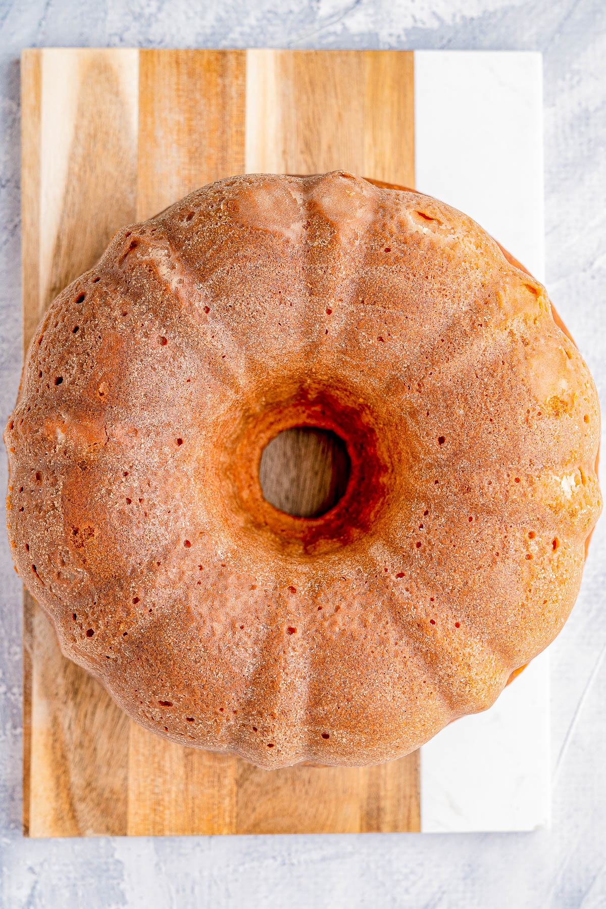 A bundt cake with a light brown crust on a wooden cutting board.