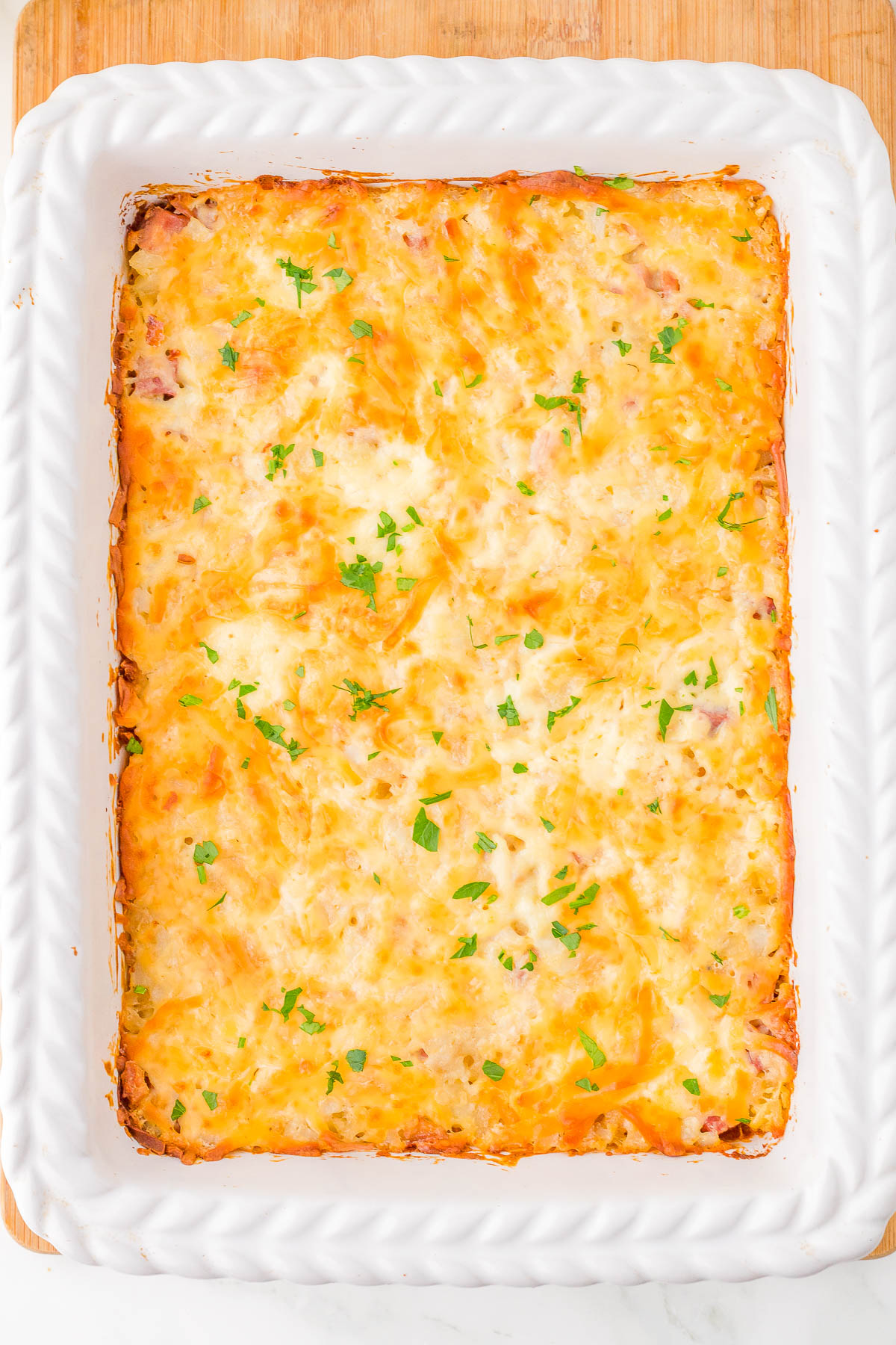 A baked casserole in a white rectangular dish, topped with melted cheese and garnished with chopped herbs.