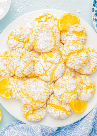 A plate of lemon crinkle cookies dusted with powdered sugar, garnished with lemon slices.