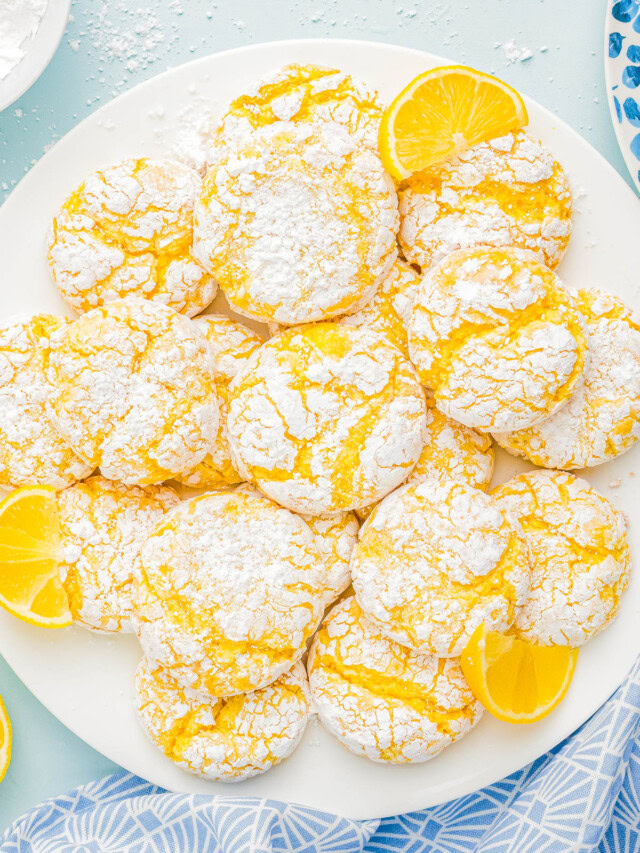 A plate of lemon crinkle cookies dusted with powdered sugar, garnished with lemon slices.