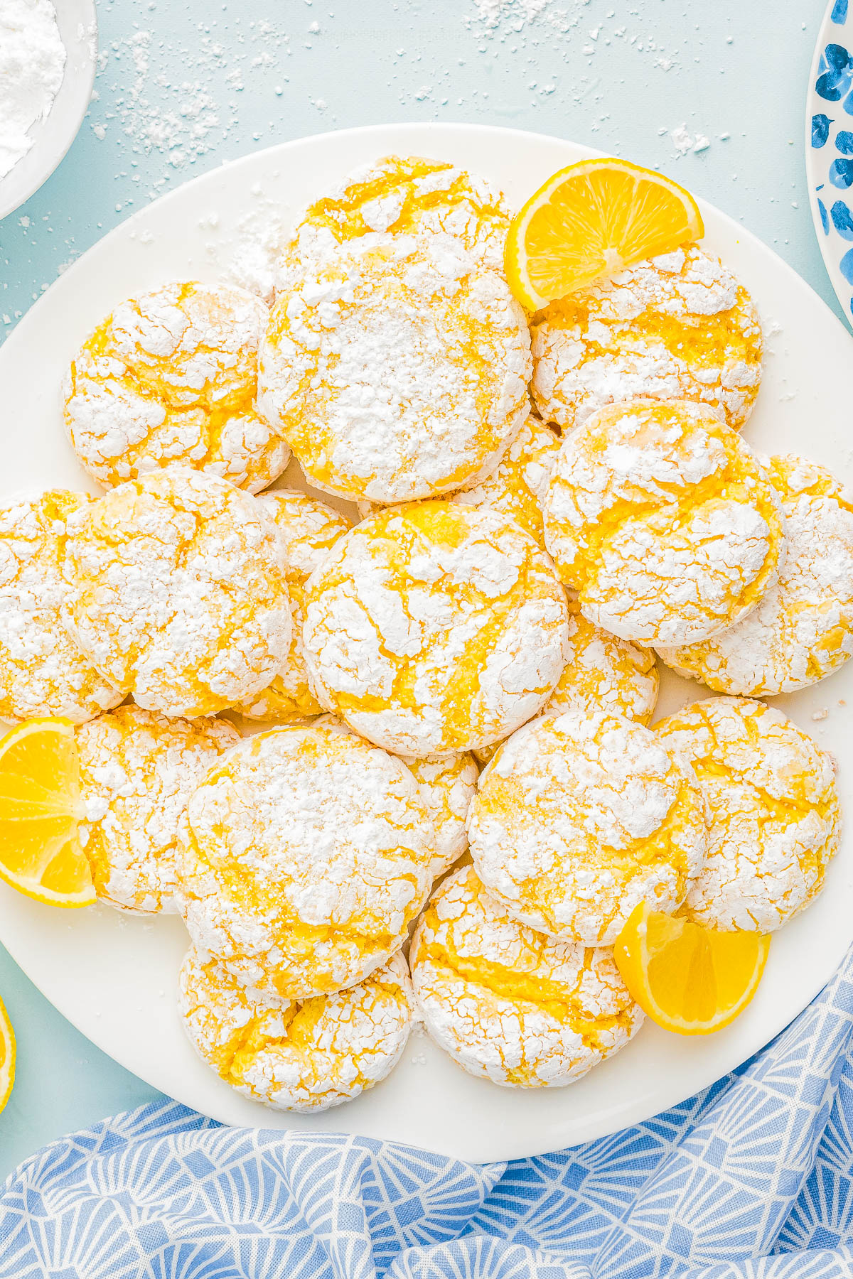 A plate of lemon crinkle cookies dusted with powdered sugar, garnished with lemon slices.