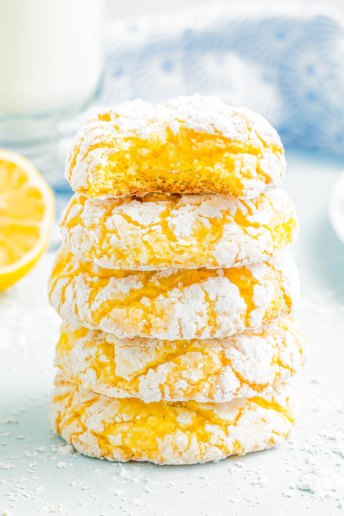 A stack of five lemon crinkle cookies dusted with powdered sugar, with one cookie showing a bite taken out.