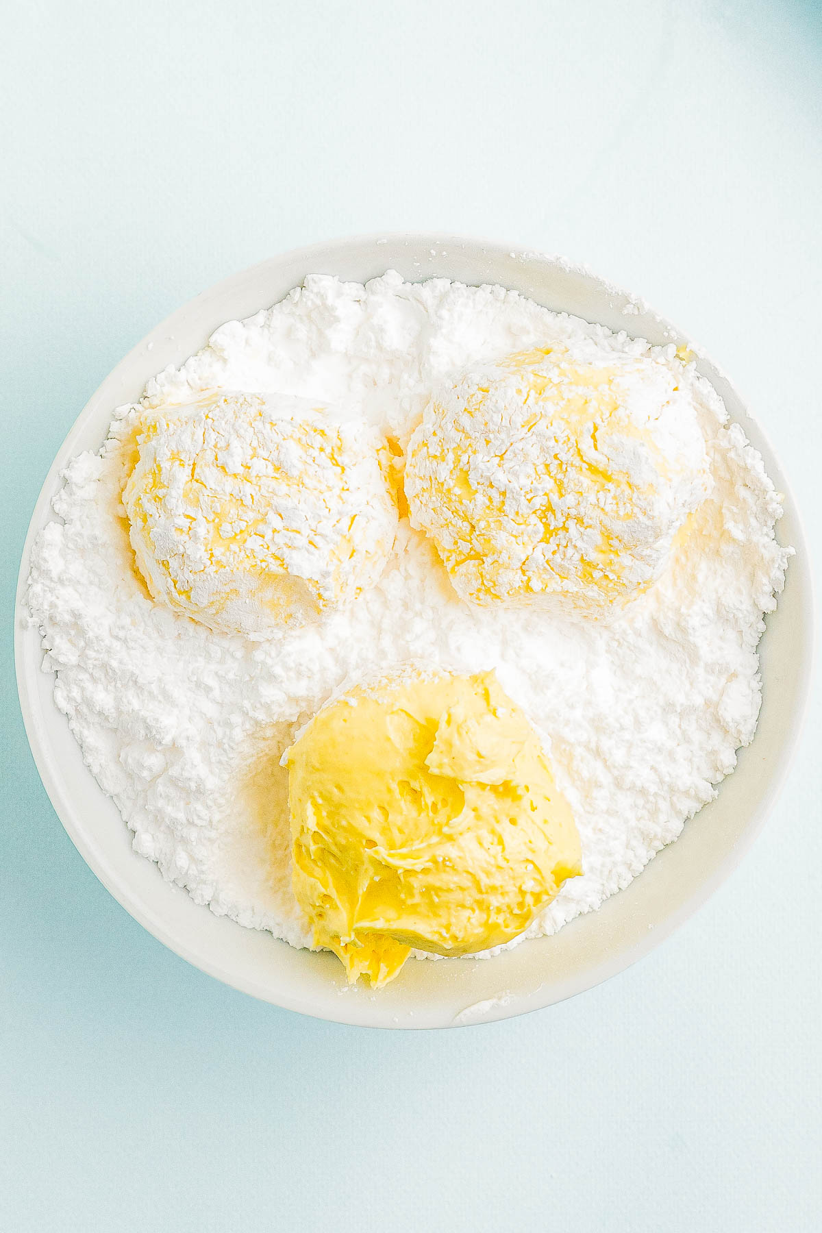 A white bowl containing powdered sugar topped with three scoops of butter or similar spread, arranged in a triangular pattern.