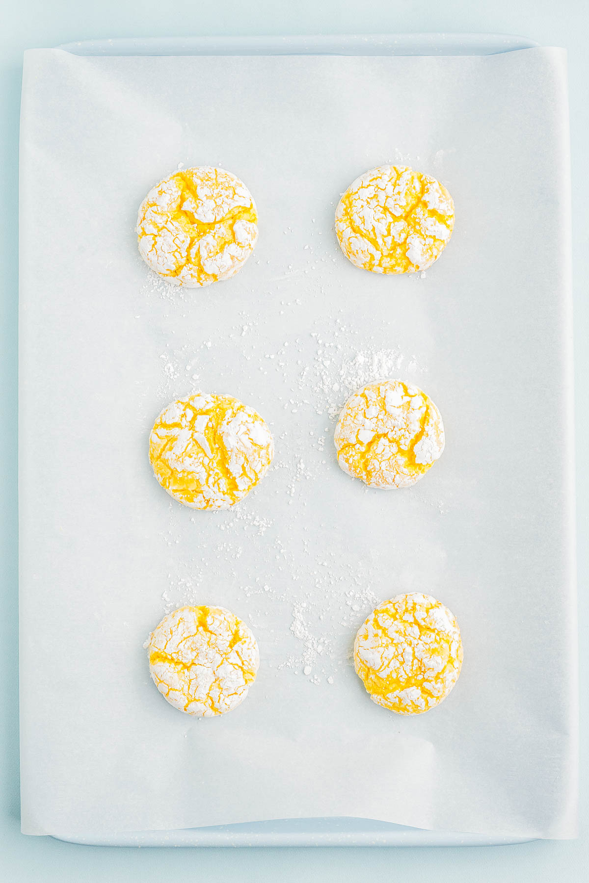 Six lemon crinkle cookies with powdered sugar on a baking sheet.