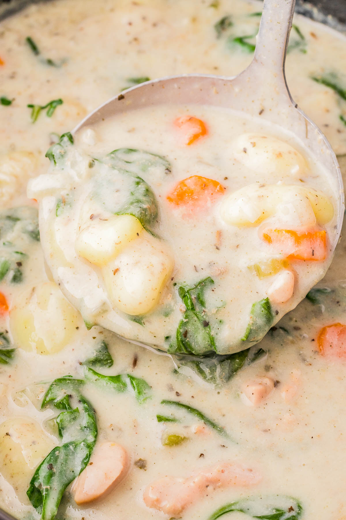 A ladle scoops creamy soup with spinach, carrot slices, and chunks of potato.