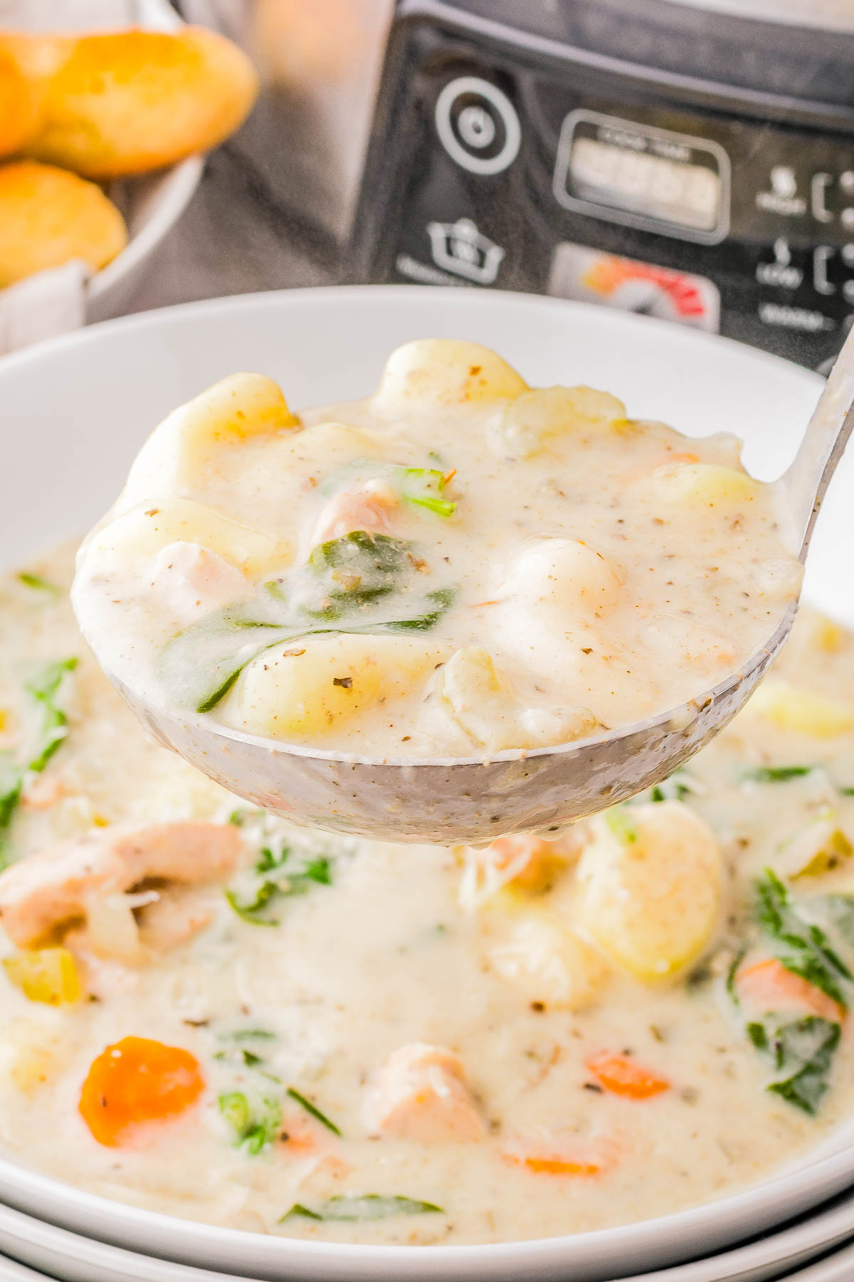 A ladle serving creamy chicken gnocchi soup with vegetables and herbs from a pot.