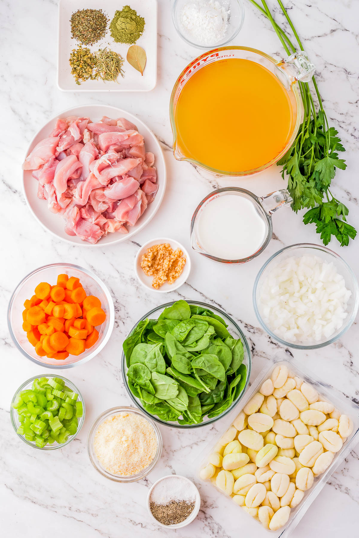 Ingredients laid out on a marble countertop include chicken pieces, baby potatoes, spinach, carrots, celery, onion, garlic, parsley, broth, herbs, milk, and seasonings.