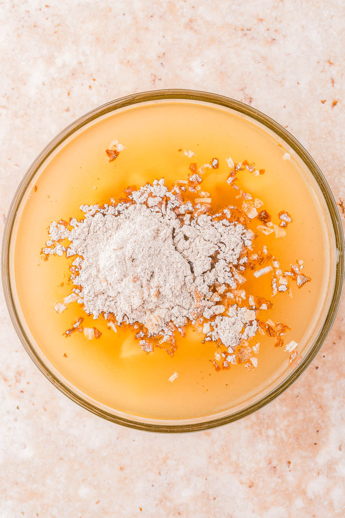 A bowl with liquid, wheat flour, and chopped nuts, viewed from above on a light surface.