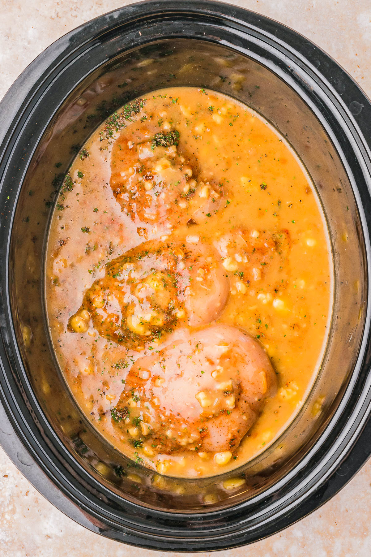 Three pieces of meat in a slow cooker with a thick, orange sauce containing herbs and corn.