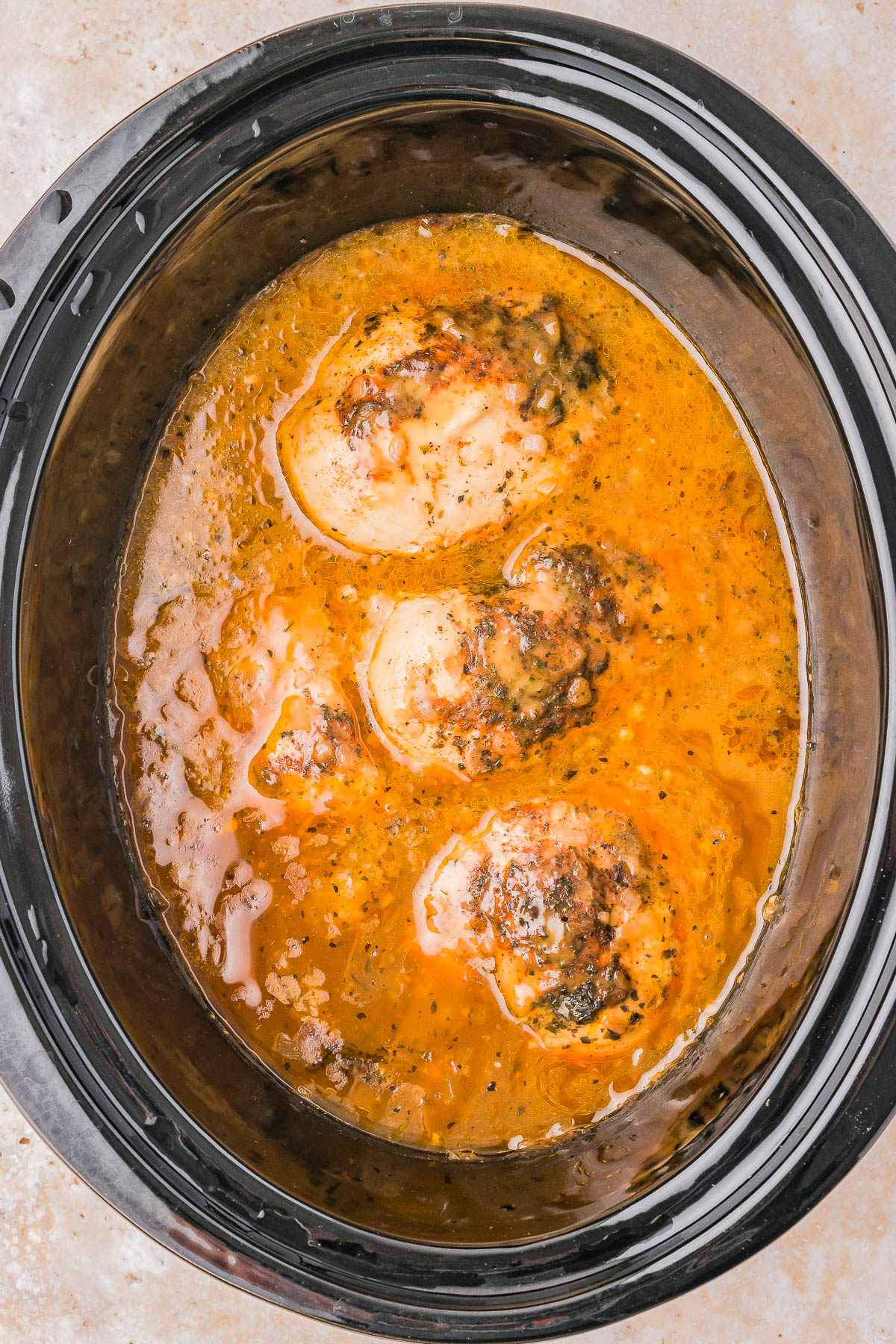 Four chicken breasts in a slow cooker with orange-brown sauce.