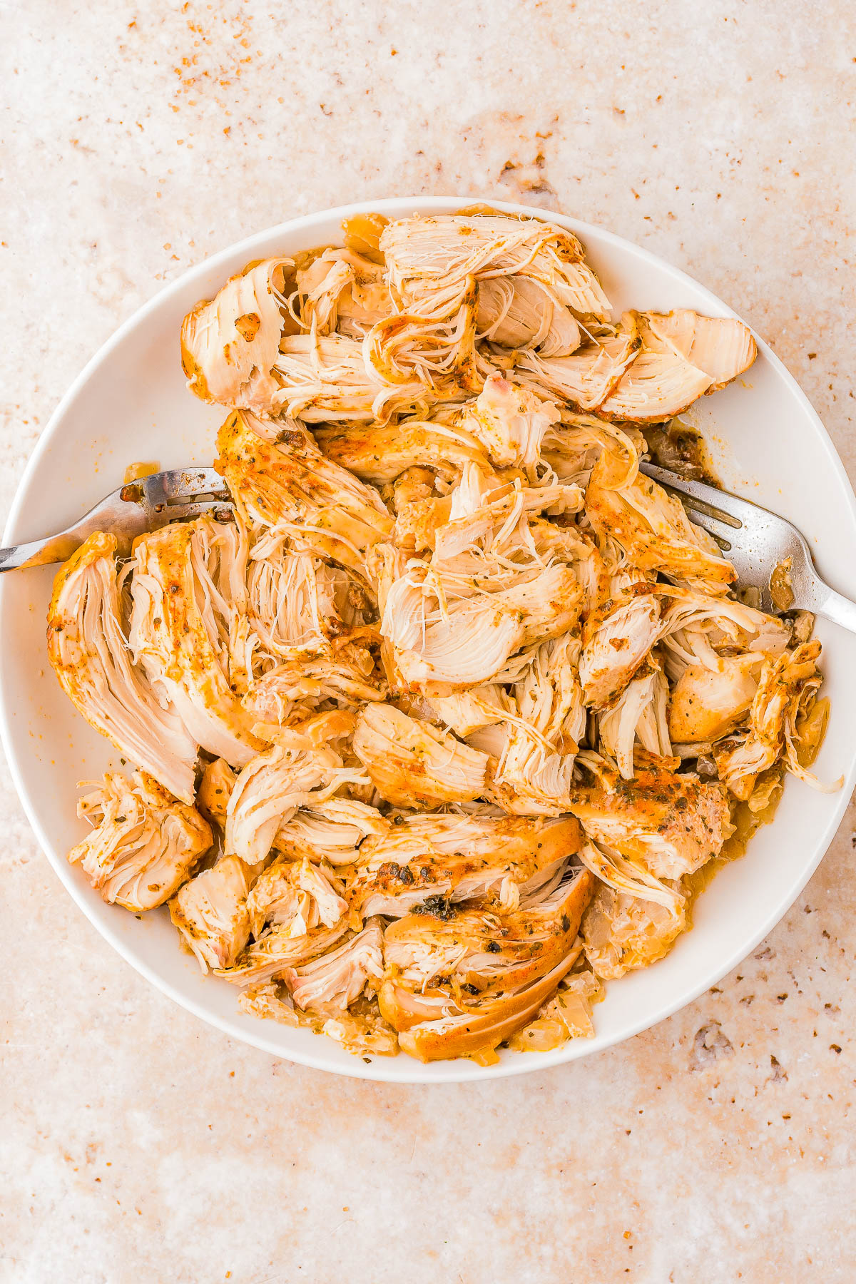 A bowl of shredded seasoned chicken with two forks on a light-colored surface.