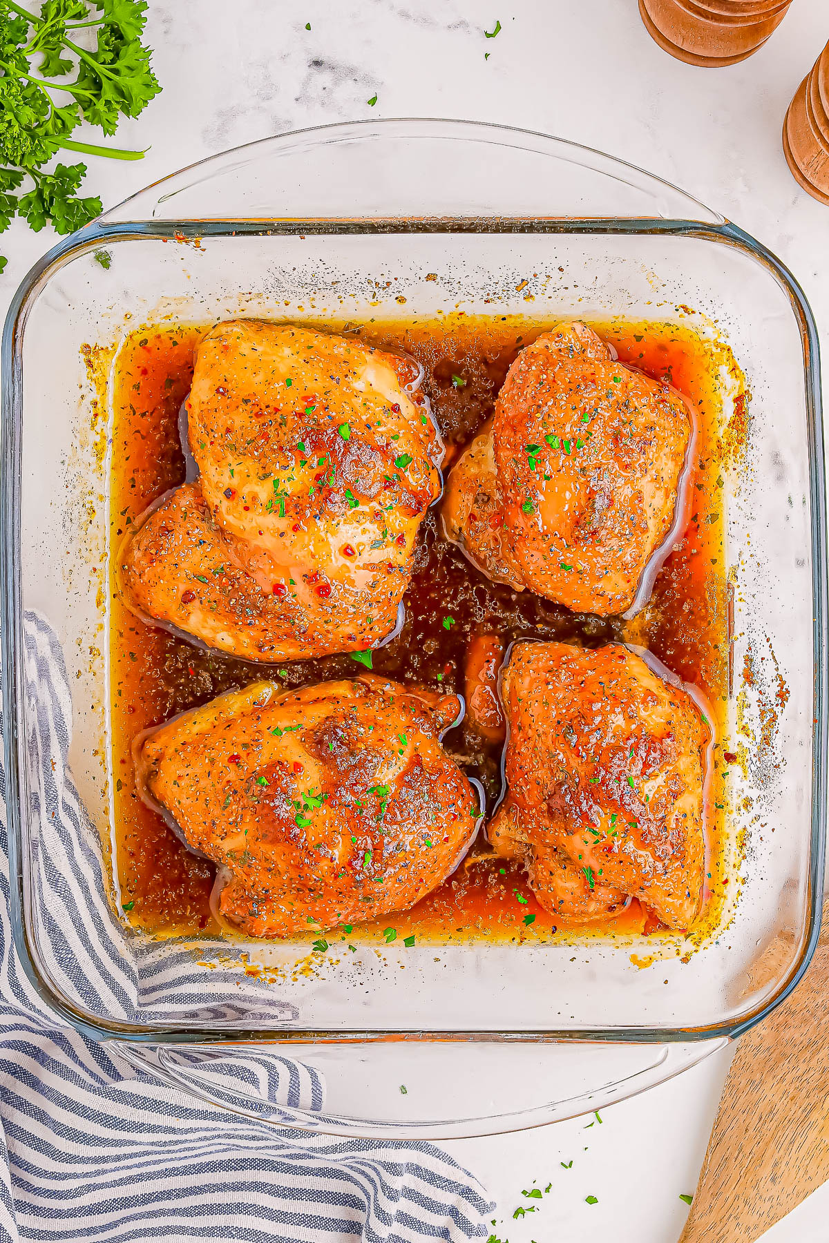 Four seasoned chicken thighs in a glass baking dish with sauce, garnished with parsley.