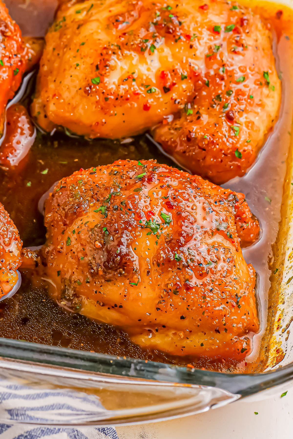 Close-up of glazed, seasoned chicken thighs in a baking dish, covered in a rich, shiny sauce.