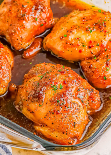 Close-up of four glazed and seasoned chicken thighs in a glass baking dish.