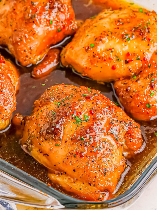 Close-up of four glazed and seasoned chicken thighs in a glass baking dish.