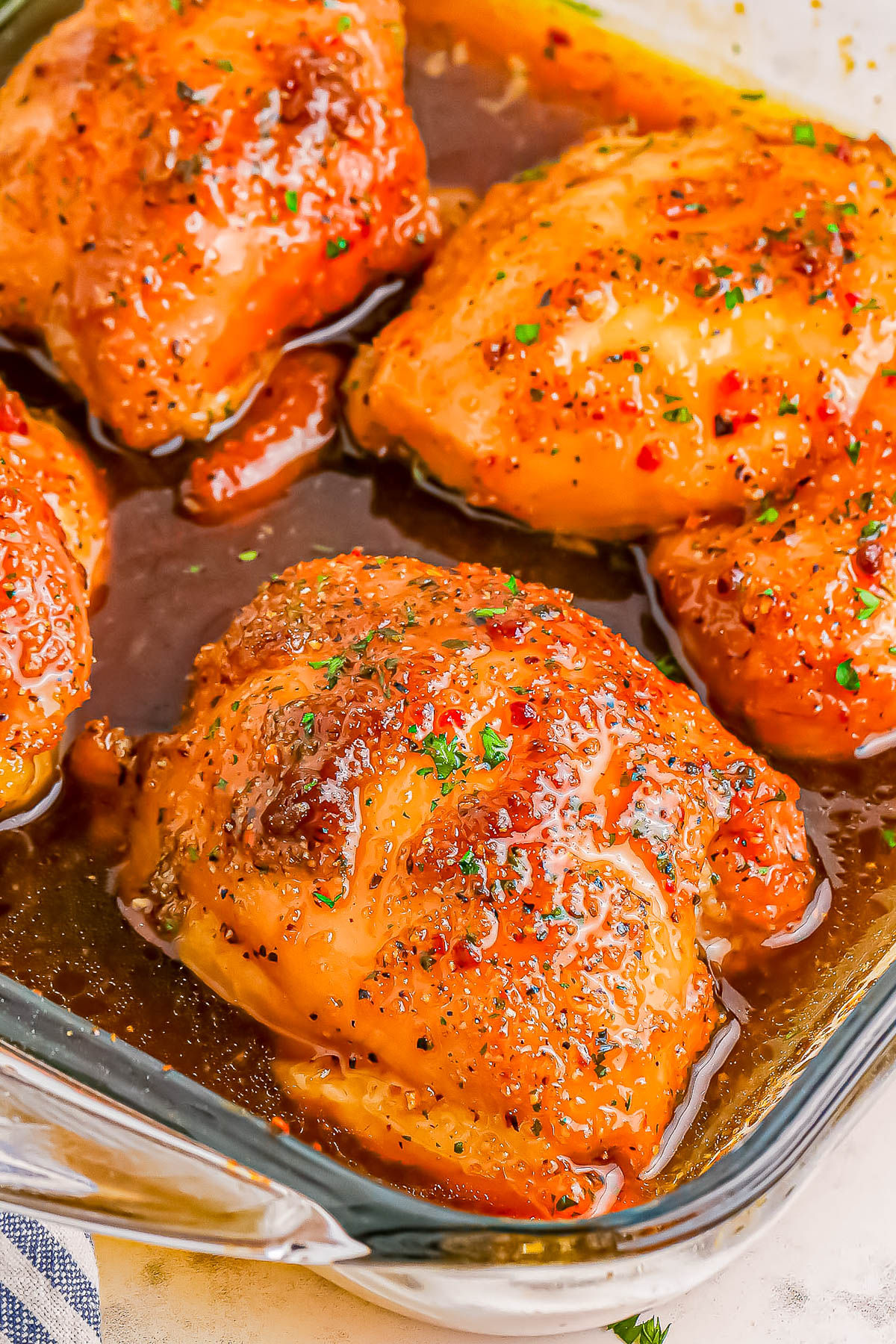 Close-up of four glazed and seasoned chicken thighs in a glass baking dish.