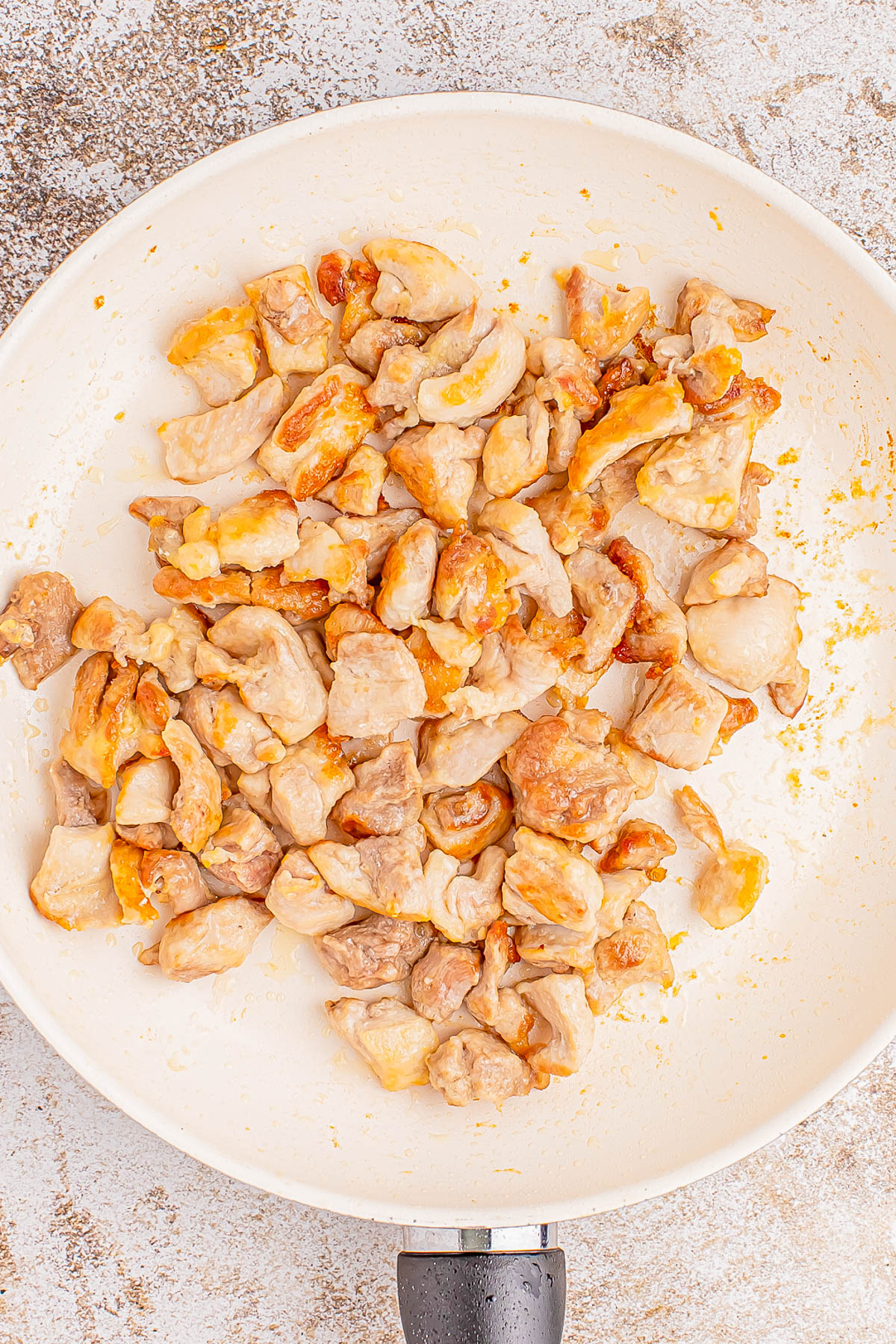 Cooked diced chicken pieces in a white frying pan.