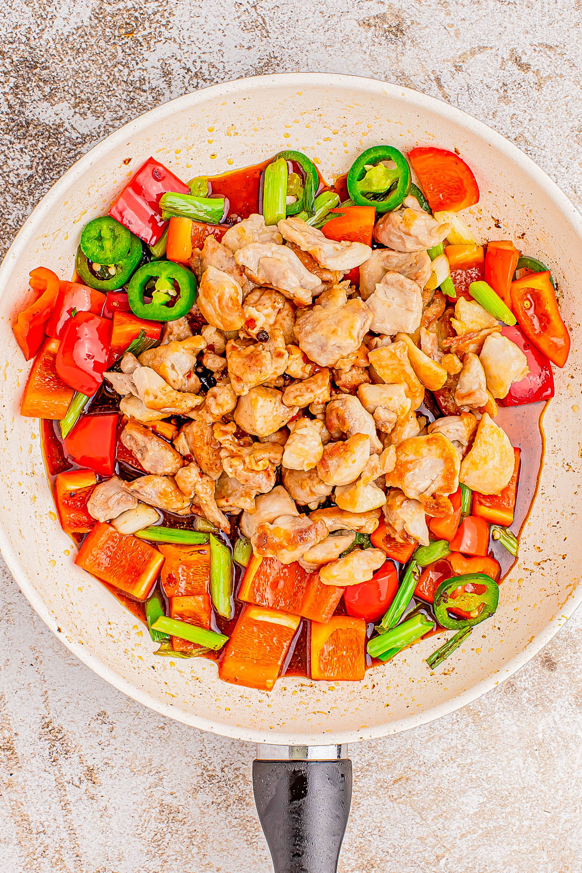 A pan filled with cooked chicken pieces, sliced bell peppers, green onions, and sliced jalapeños.