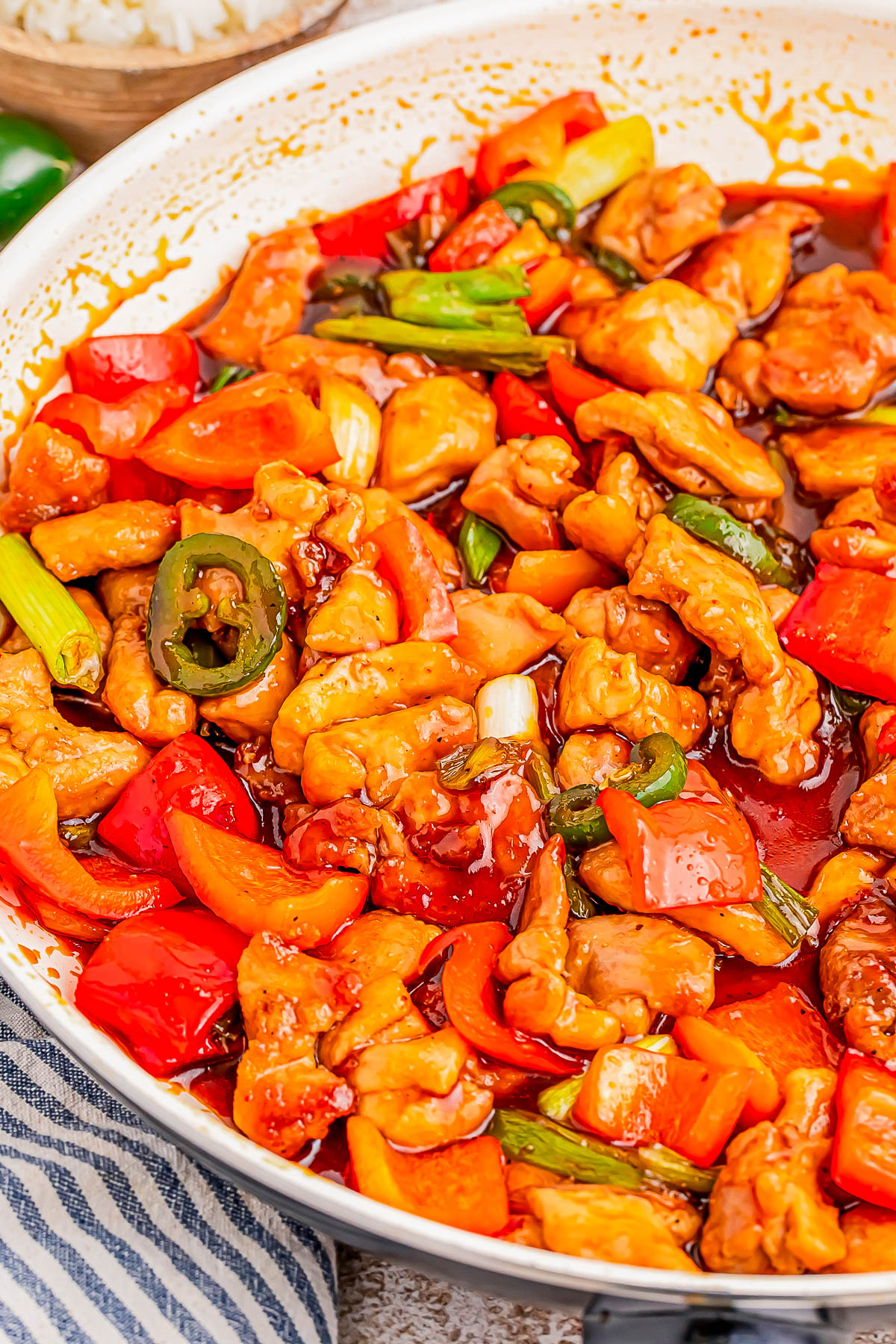 A skillet filled with cooked chicken pieces, red and orange bell peppers, sliced green onions, and a glossy sauce.