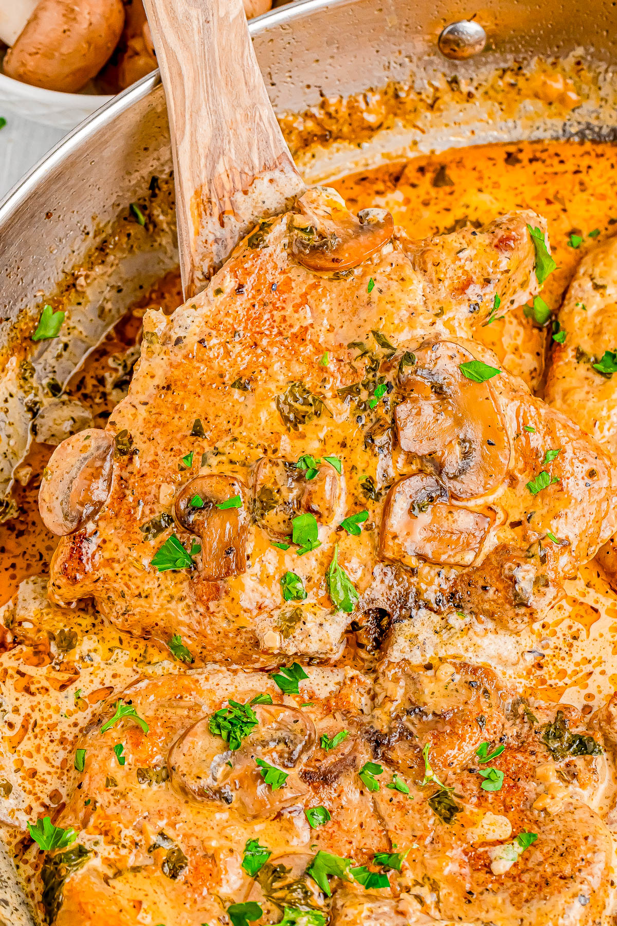 Chicken breasts in a creamy mushroom sauce with herbs in a skillet, garnished with chopped parsley.