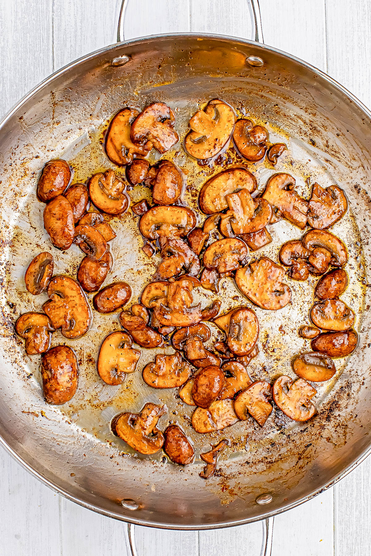 Sautéed mushrooms in a large silver skillet on a light wooden surface.