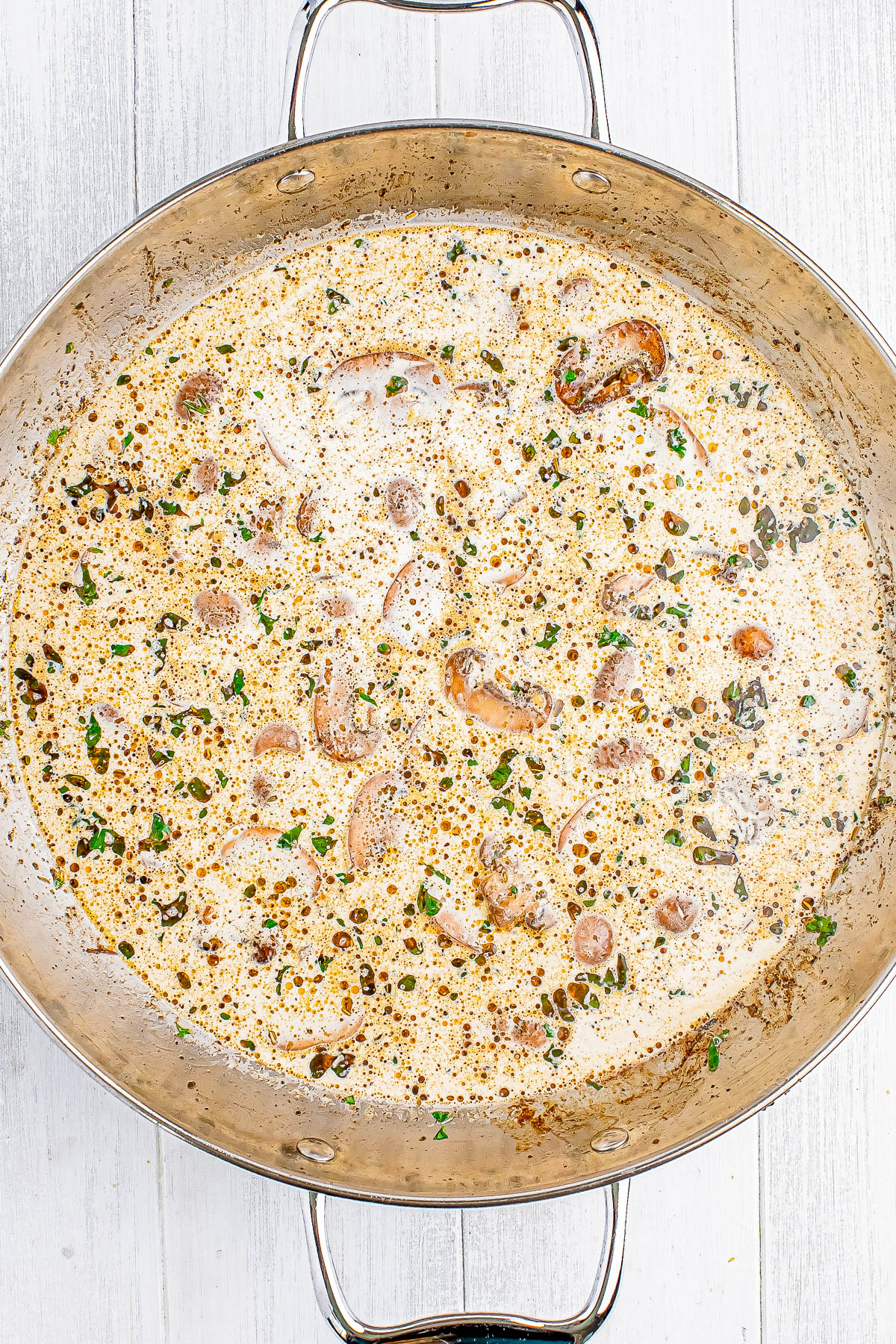 A large metal pan filled with a creamy mushroom sauce, topped with herbs, on a light wooden surface.