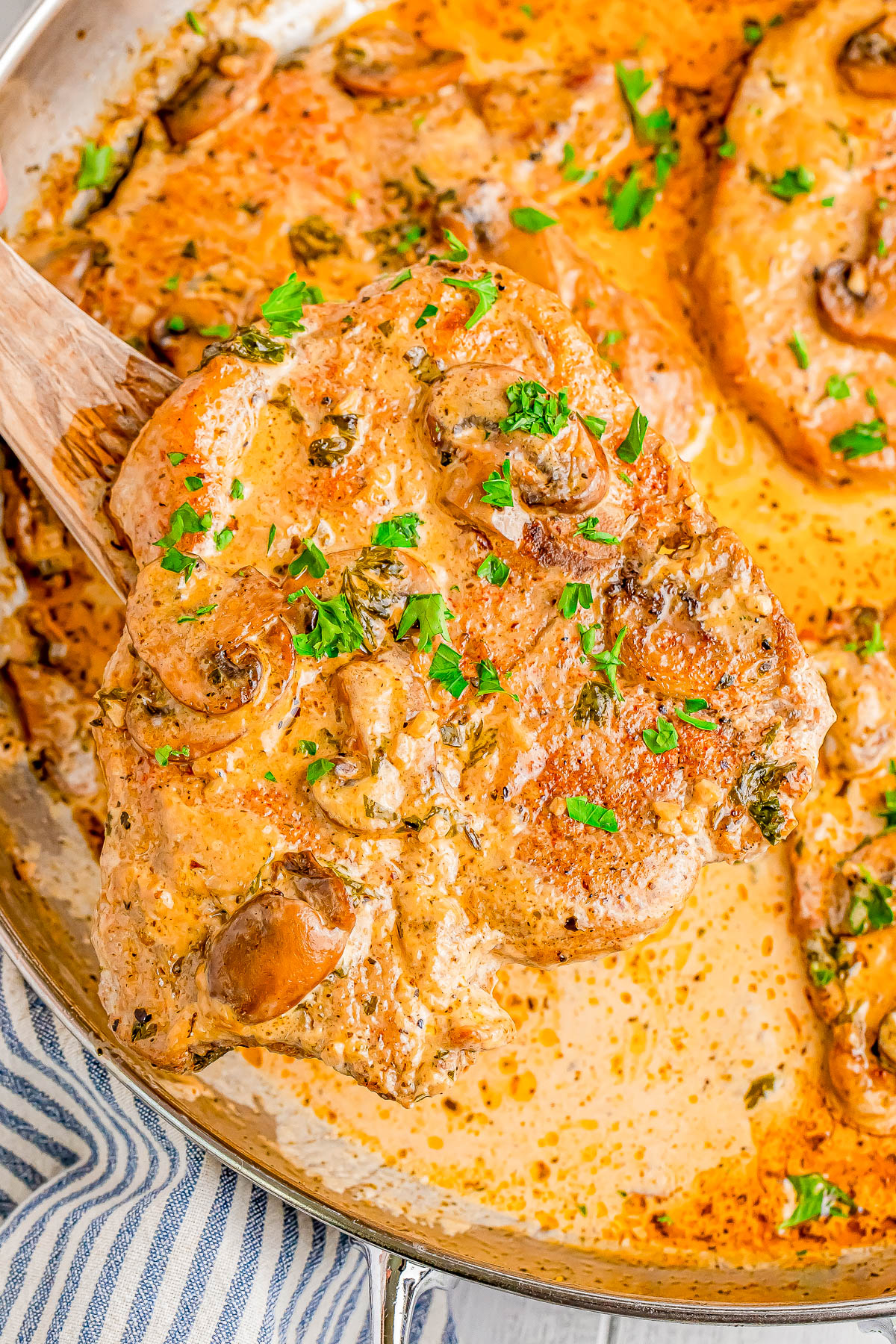 Cooked pork chops in a creamy mushroom sauce garnished with parsley in a pan.